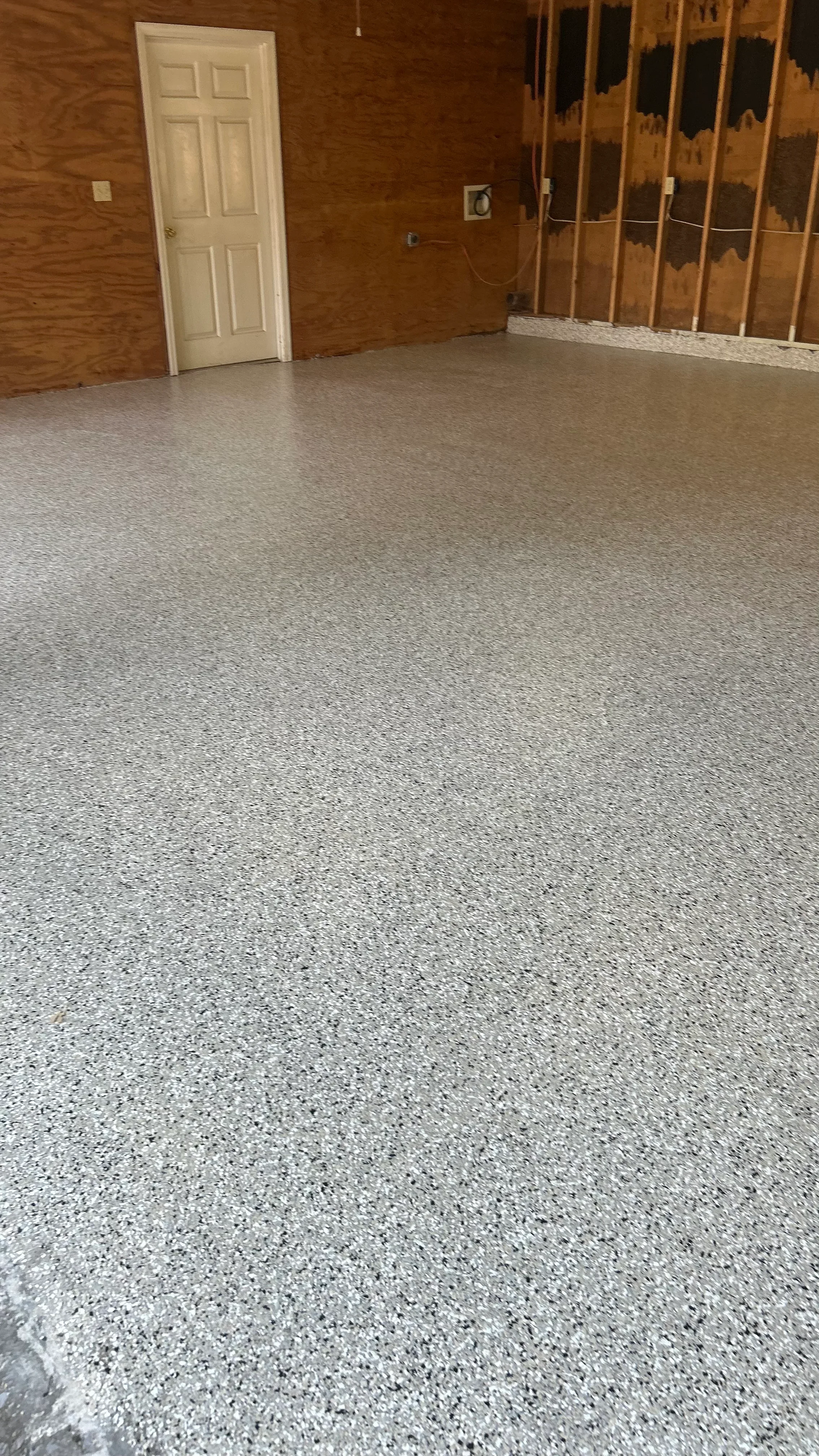 Gray speckled epoxy coating on concrete garage floor with white trim and framed walls