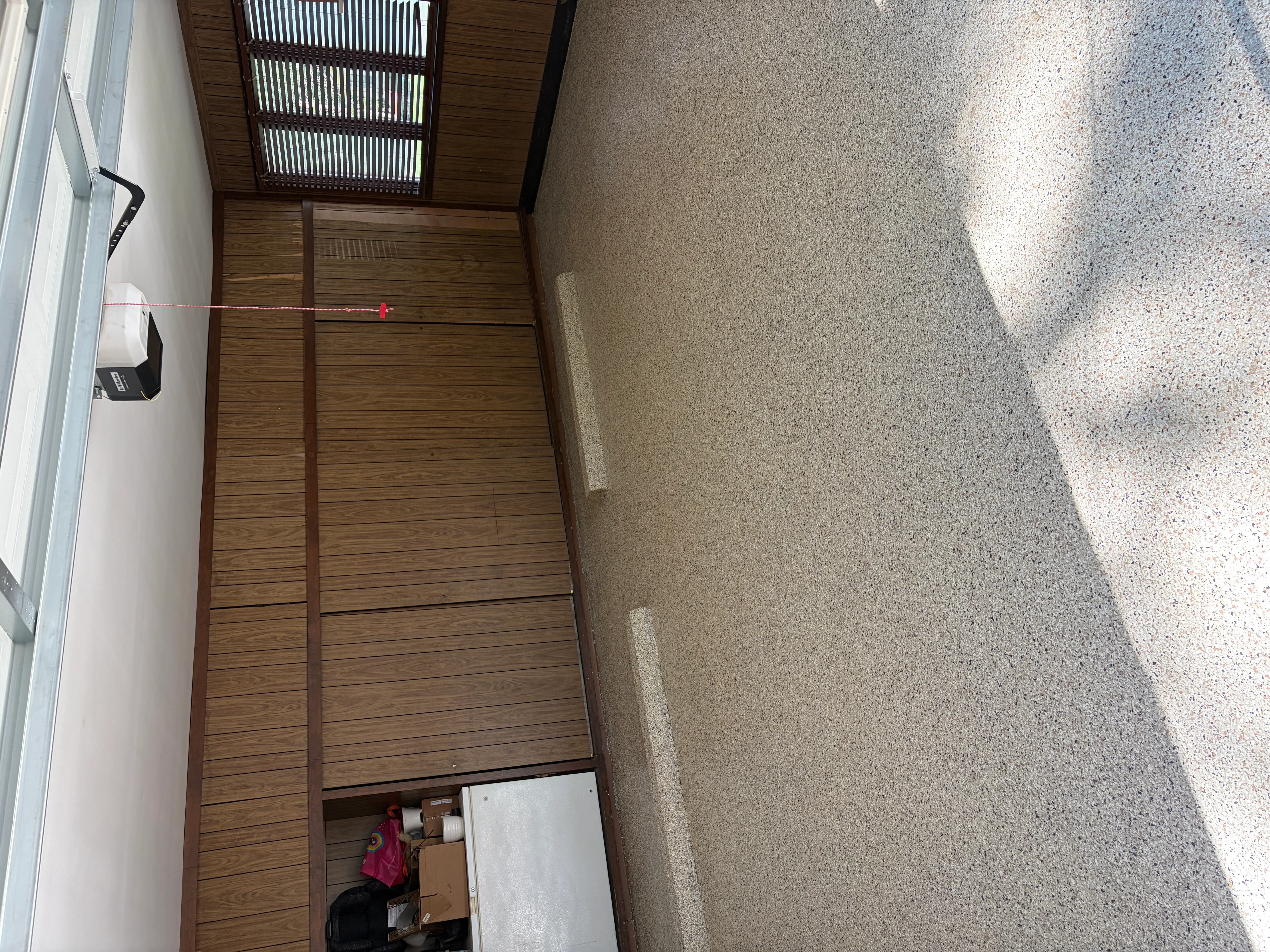 Finished concrete patio with aggregate texture next to wooden deck and white wall