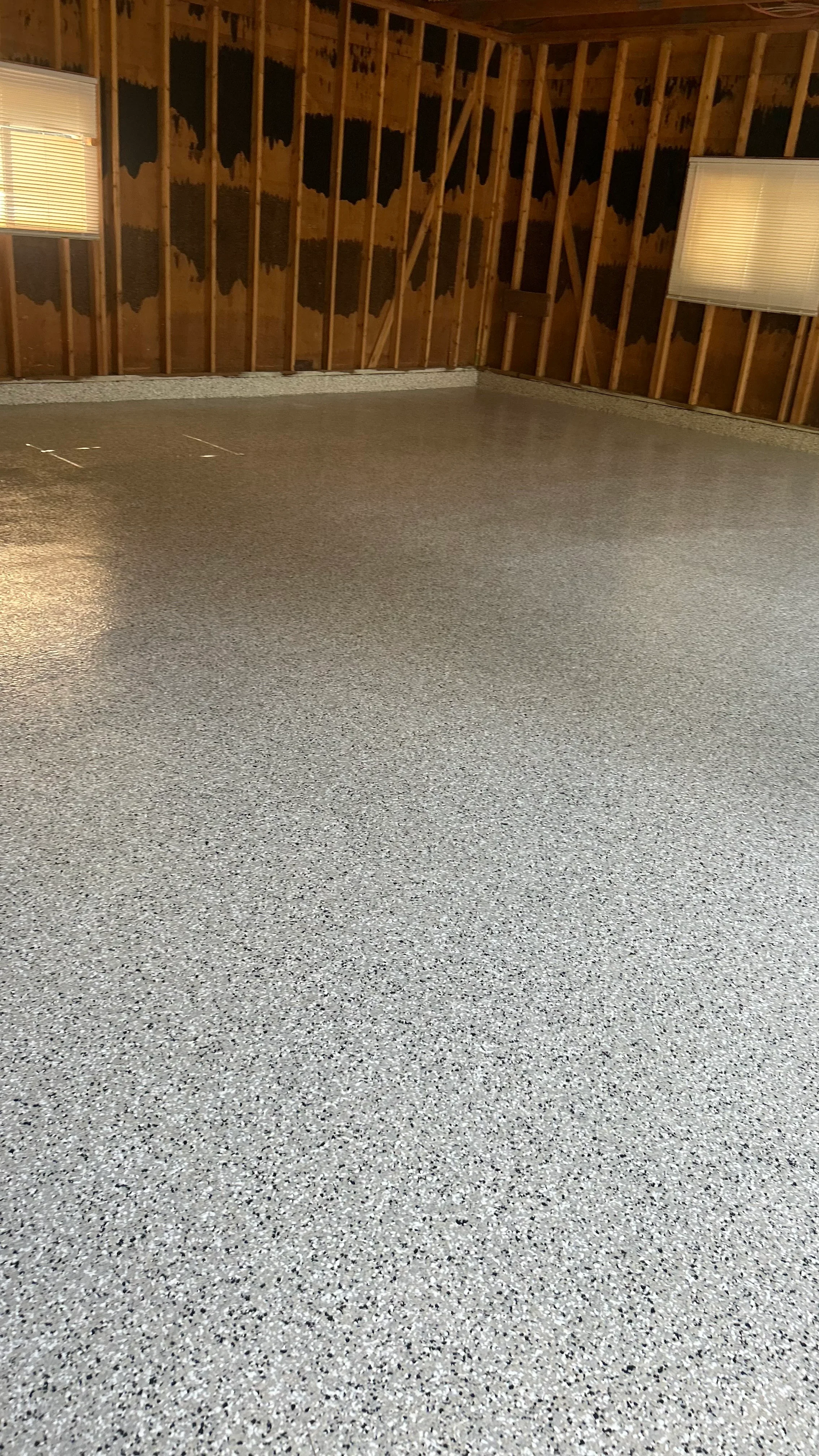 Light gray speckled epoxy floor coating in garage with wood framing and recessed lights