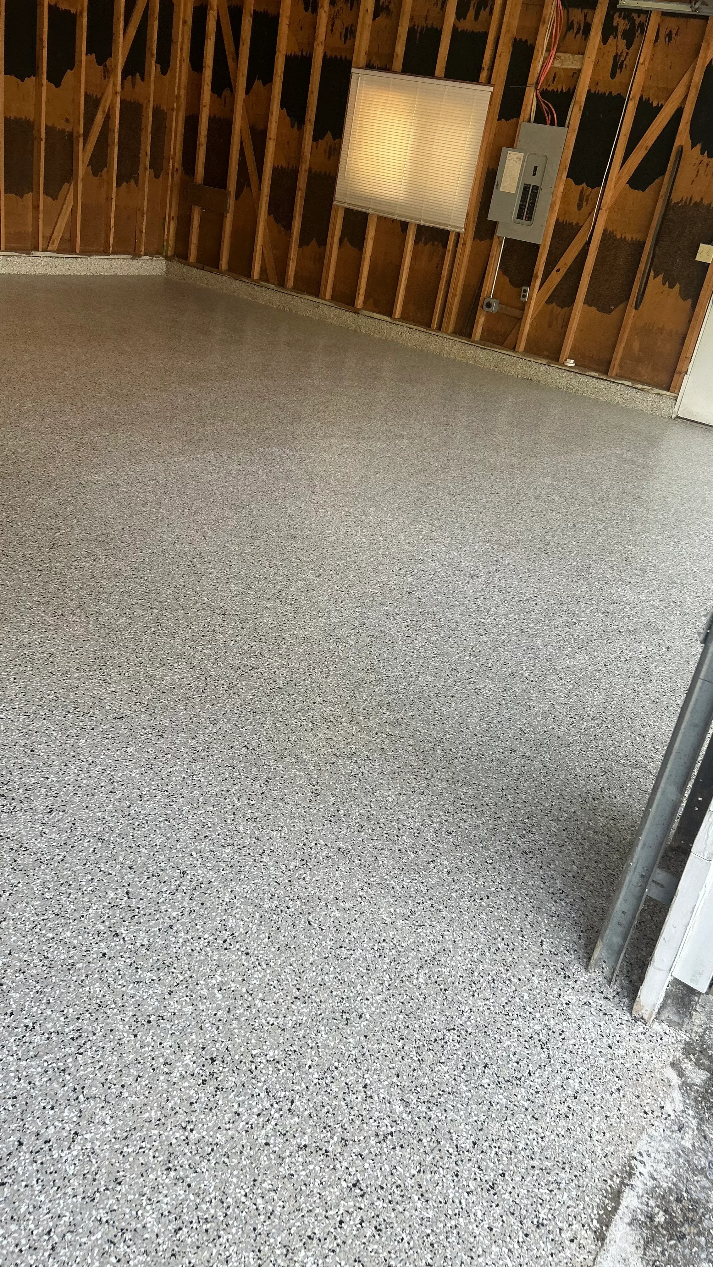 Gray speckled epoxy-coated garage floor with finished edges and framed wall framing visible
